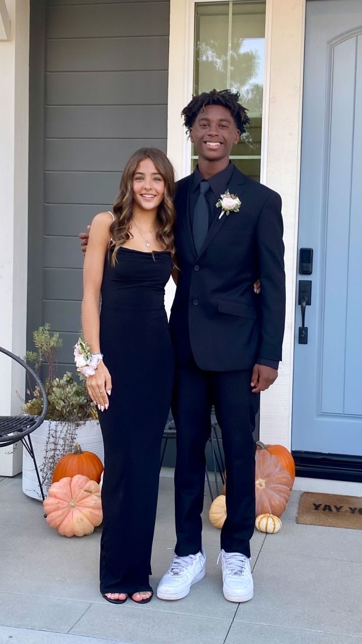 a man and woman standing in front of a house with pumpkins on the porch