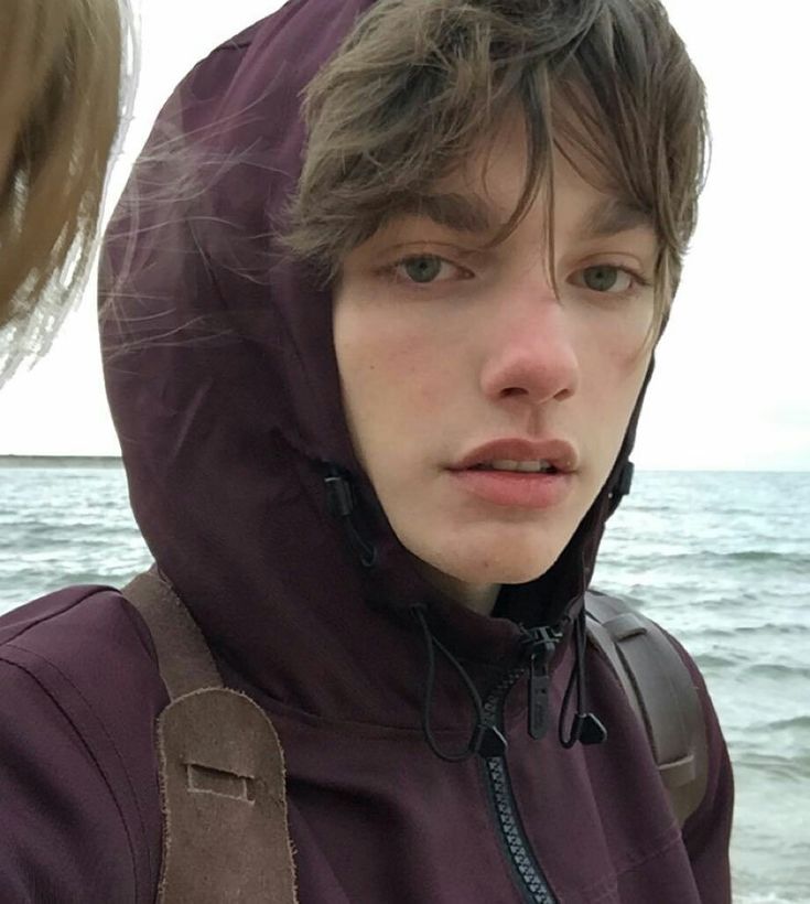 a young man wearing a purple jacket standing next to the ocean