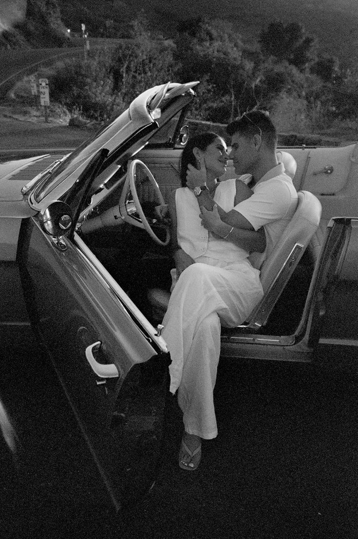 a man and woman are sitting in the back of a convertible car, with their arms around each other