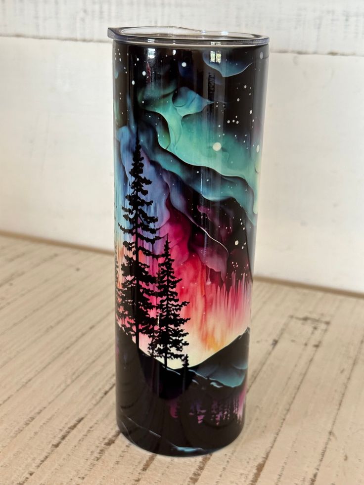 a black and purple tumbler with trees painted on the side is sitting on a wooden floor