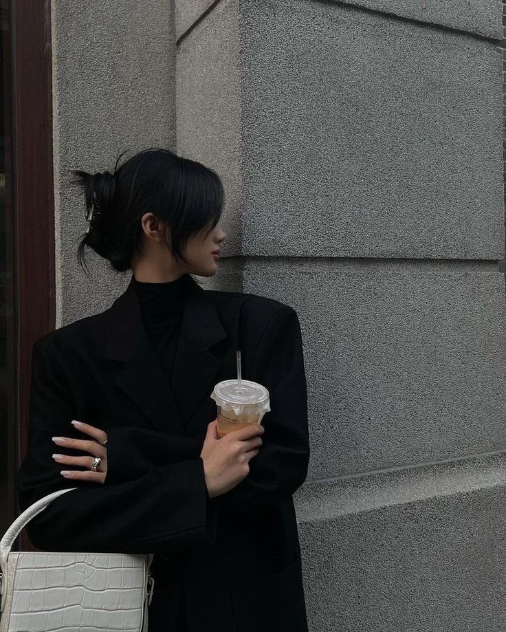 a woman holding a white bag next to a building with a cup in her hand