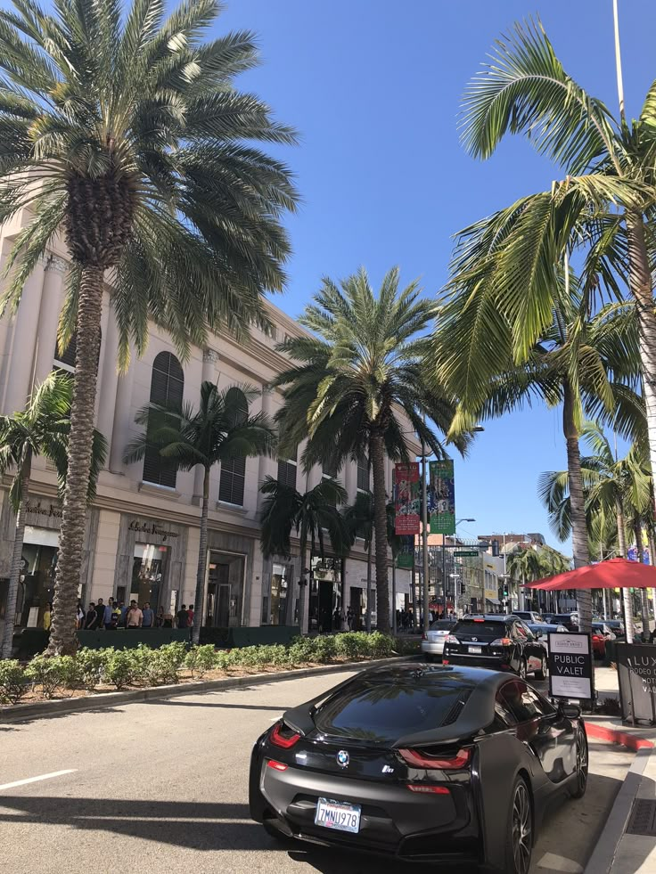 a black car parked on the side of a road next to palm trees and buildings