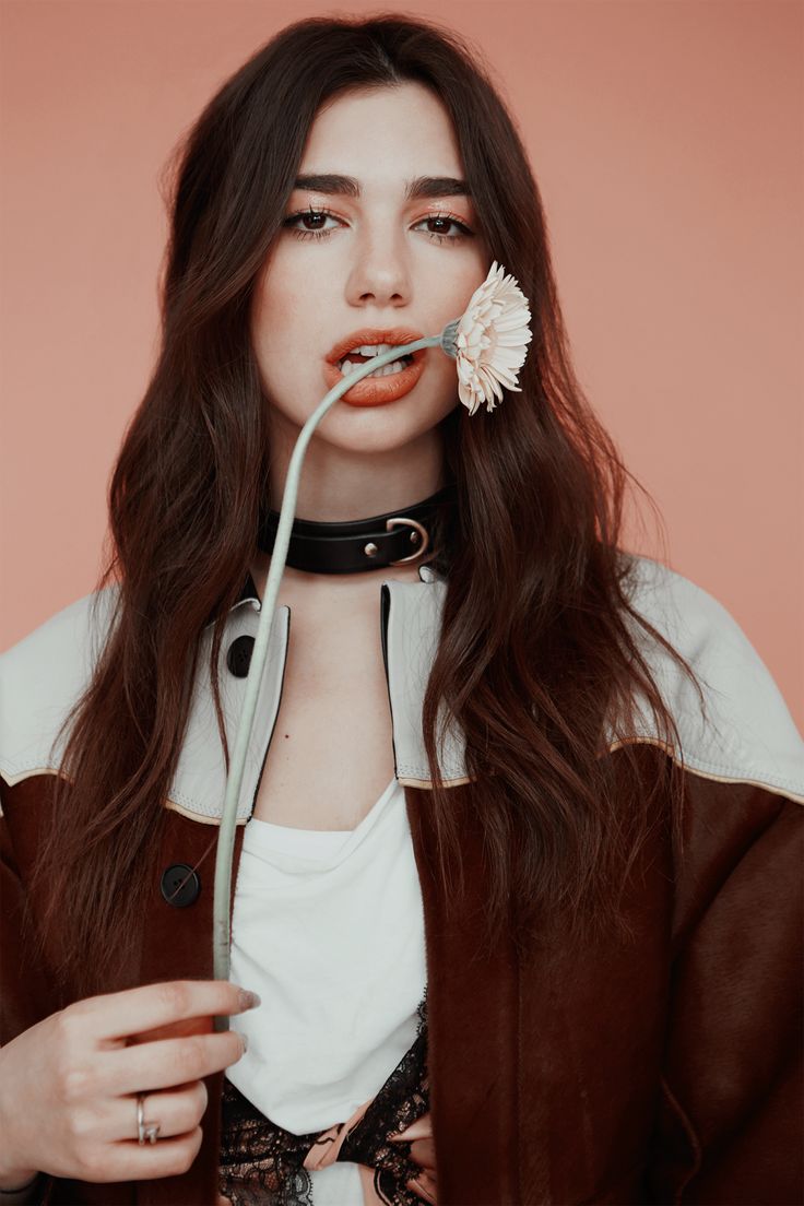 a woman holding a flower in her mouth and wearing a leather jacket with laces on it