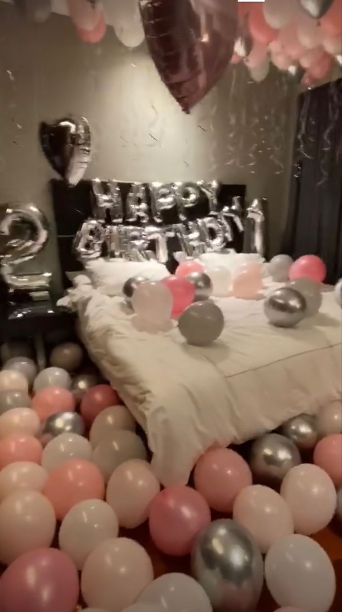 a room filled with lots of balloons and a bed covered in white sheets next to a mirror