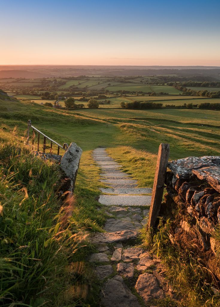 a stone path going up to the top of a hill with green fields in the background