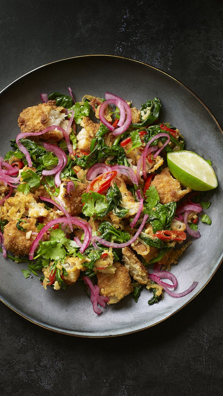 a plate full of food with onions, lettuce and chicken on it next to a lime wedge