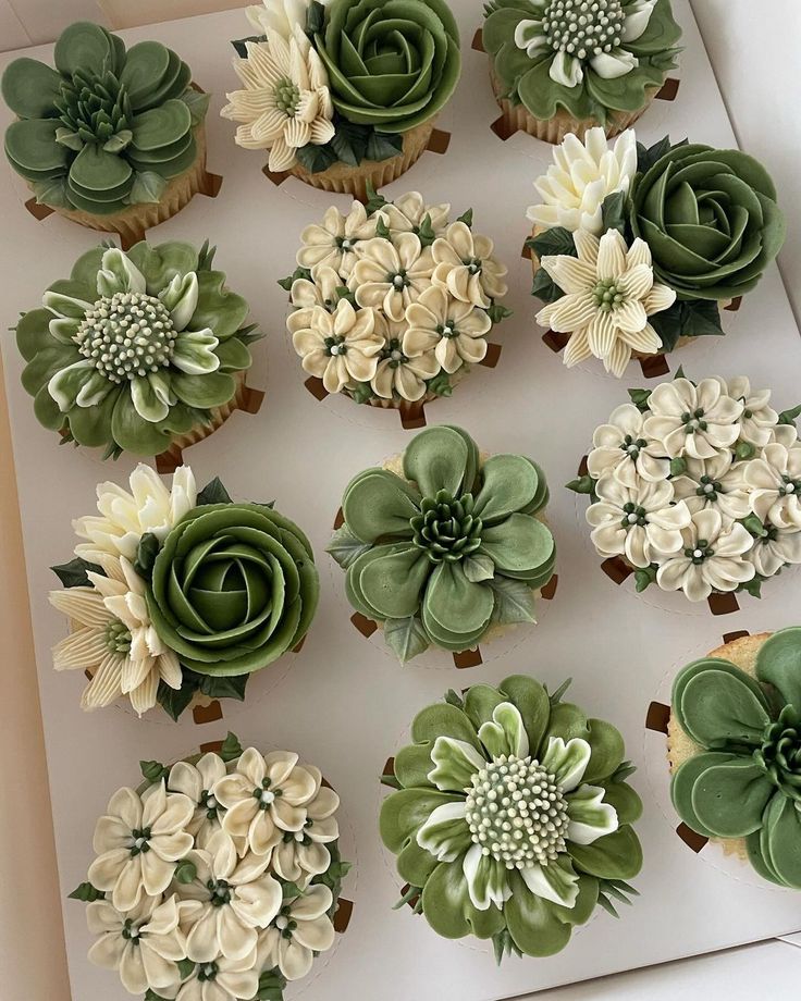 cupcakes decorated with green and white flowers are displayed in a box on a table