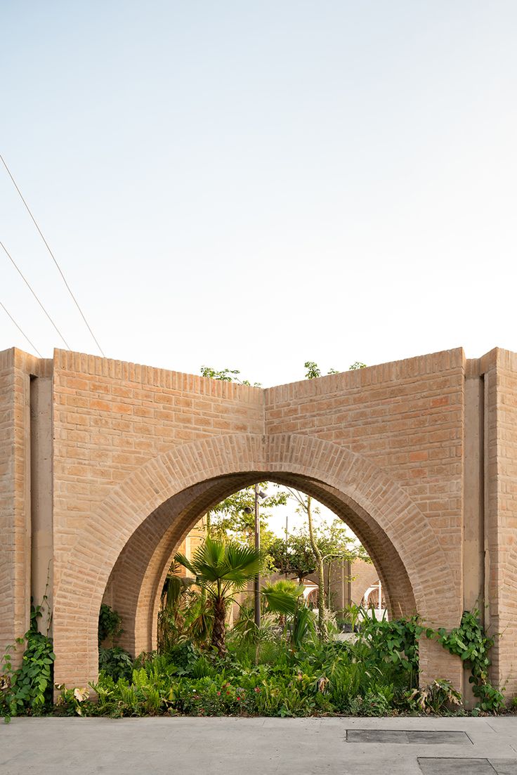 an arched brick wall with plants growing on it