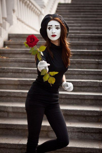 a woman with white makeup holding a rose in front of some steps and wearing gloves