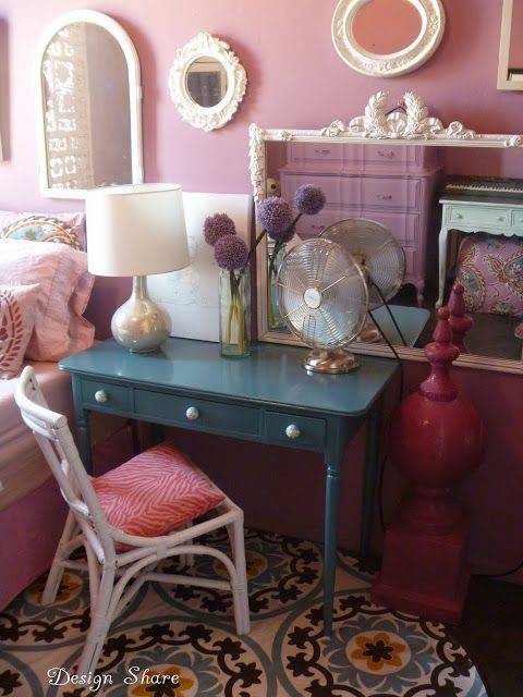 a small desk with a fan, mirror and lamp on it in a room that has pink walls