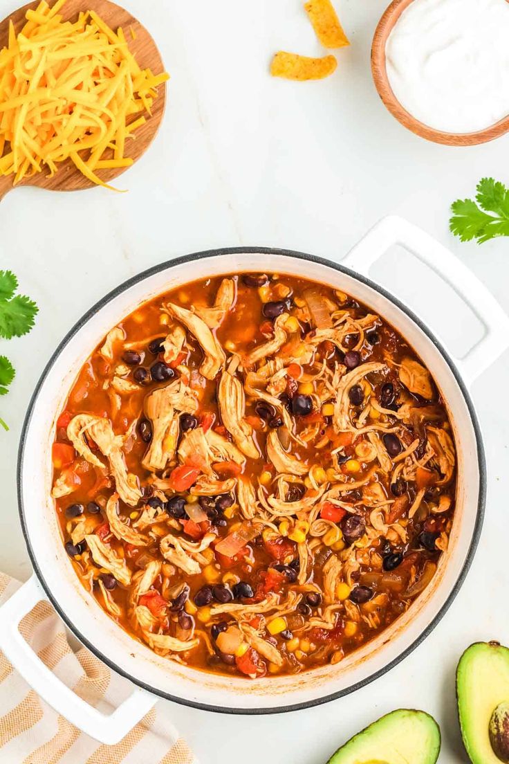 a large pot filled with chicken tortilla soup next to avocados and sour cream