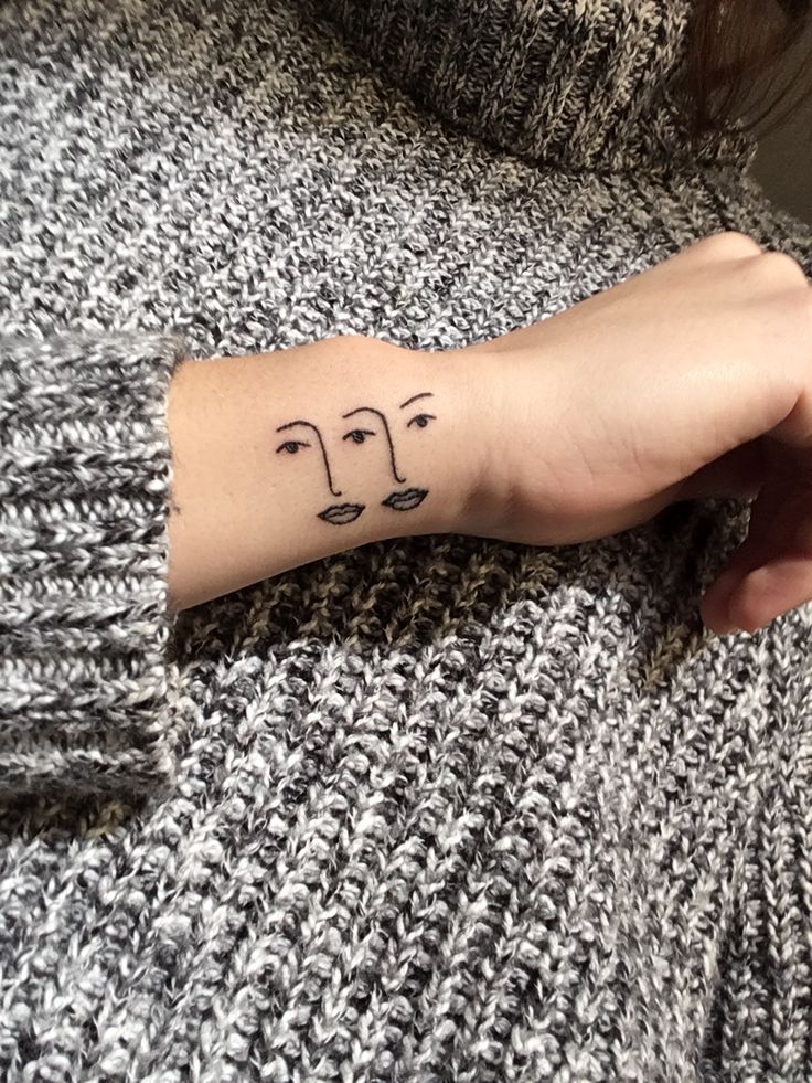 a woman's arm with a tattoo on it that has three faces drawn on it