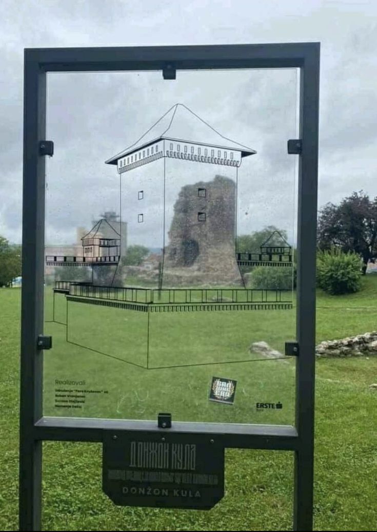 the reflection of an old castle in a glass display case on green grass with trees and buildings behind it