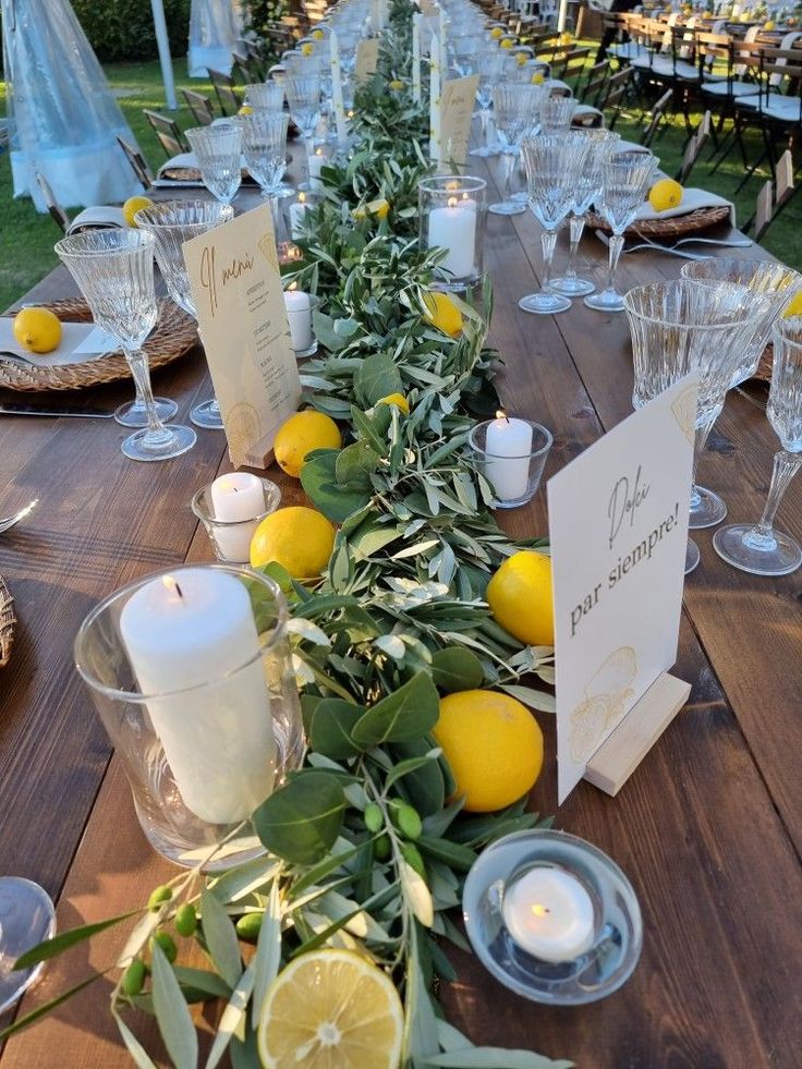 a long table with lemons, candles and place settings on it for an outdoor dinner