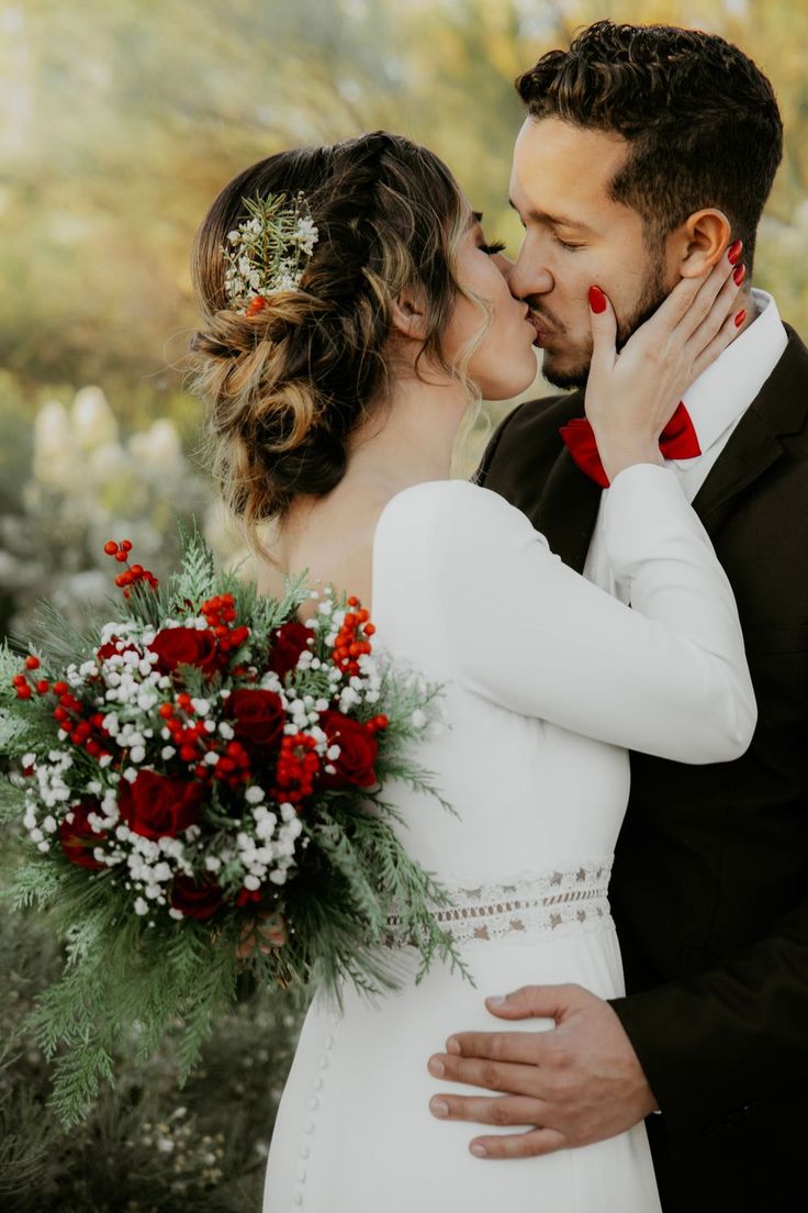 a bride and groom kissing each other in front of trees with red berries on them