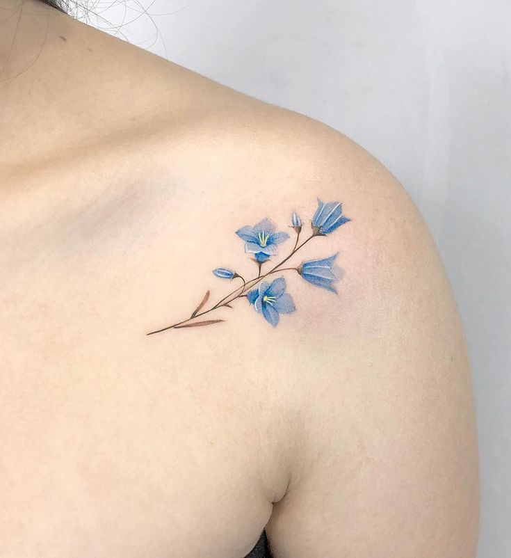 a blue flower tattoo on the back of a woman's shoulder