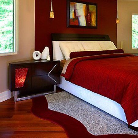 a bedroom with red walls and white bedding, hardwood flooring, and two windows