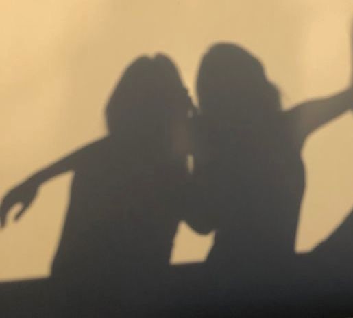 the shadow of two people holding their arms out in front of a white wall with shadows on it