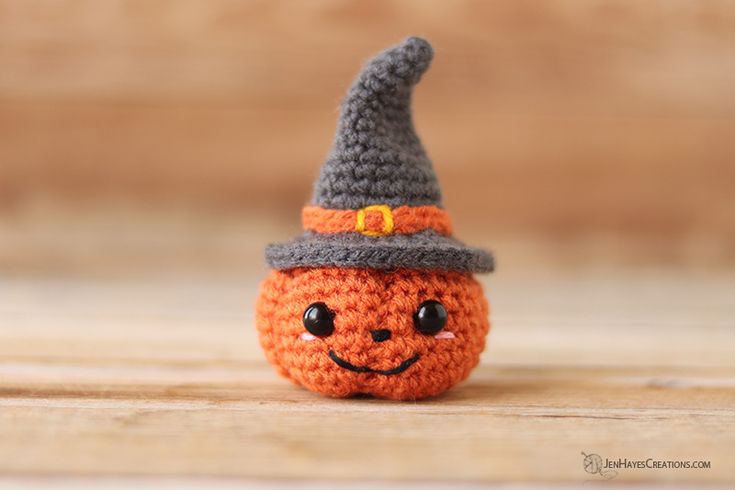 an orange crocheted pumpkin with a hat on it's head sitting on a wooden surface