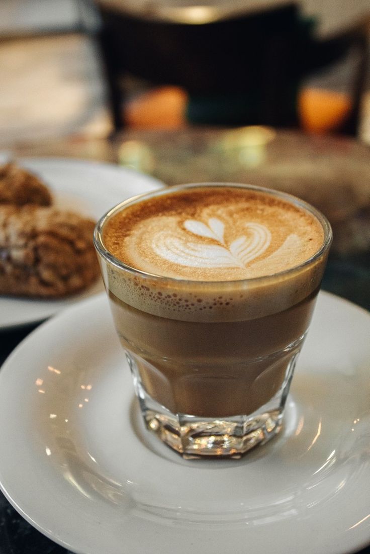 a cappuccino on a saucer next to cookies and a glass of coffee