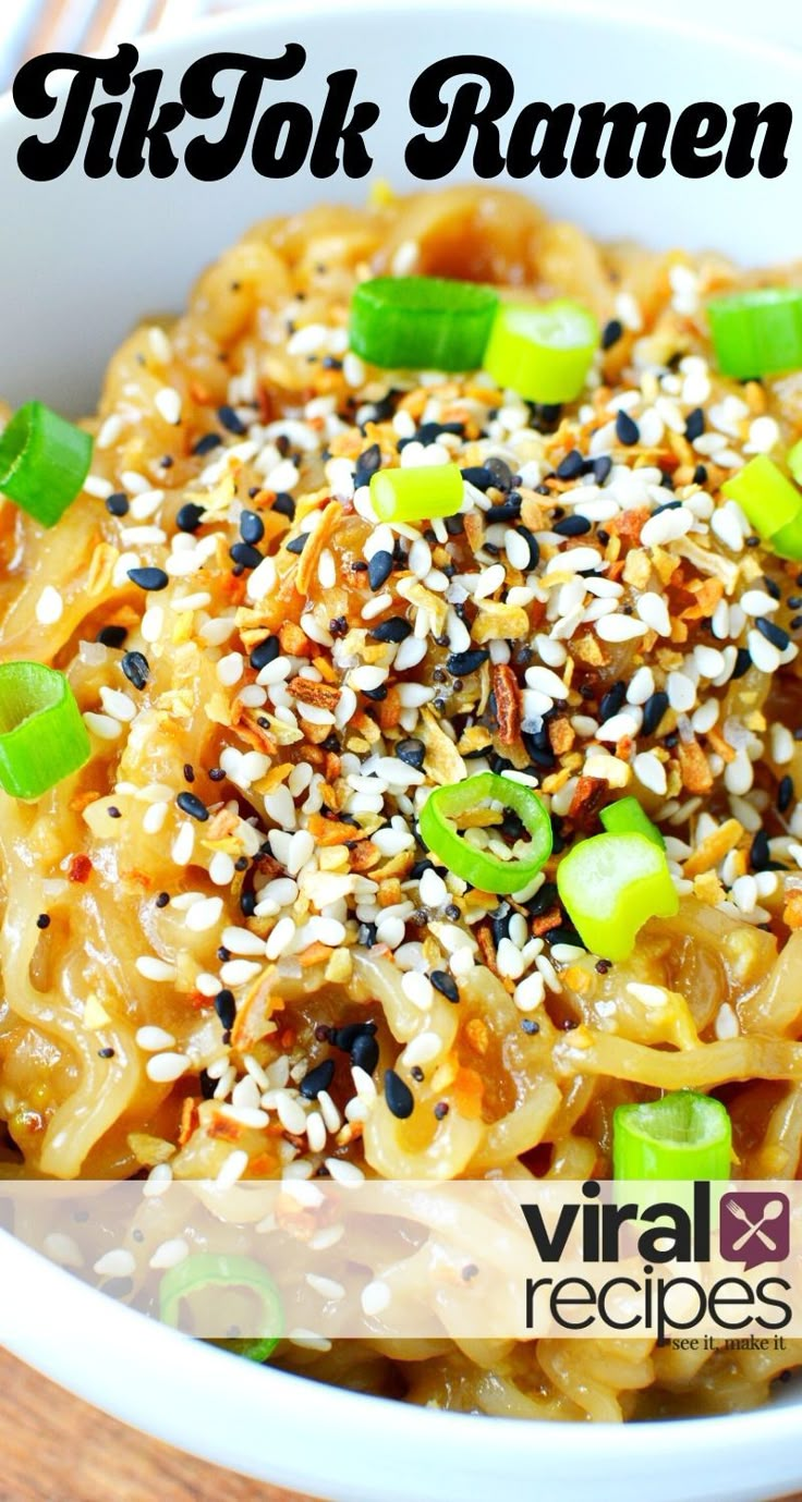 a white bowl filled with noodles covered in sesame seeds and chopped green onions on top