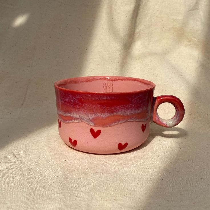 a pink cup with hearts painted on the outside and inside sitting on a white surface