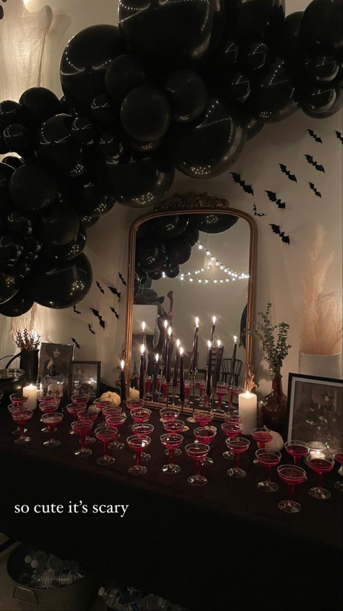 a table topped with lots of black balloons and candles next to a mirror filled with wine glasses