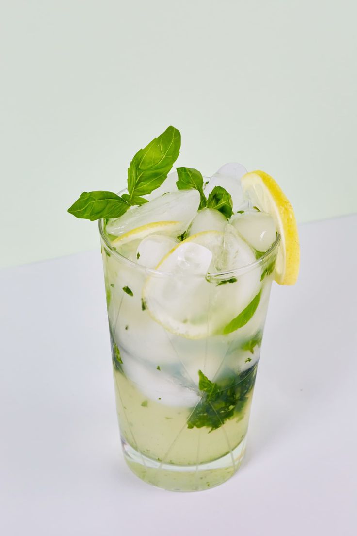 a mojito with mint and lemon on a white table next to a lime slice