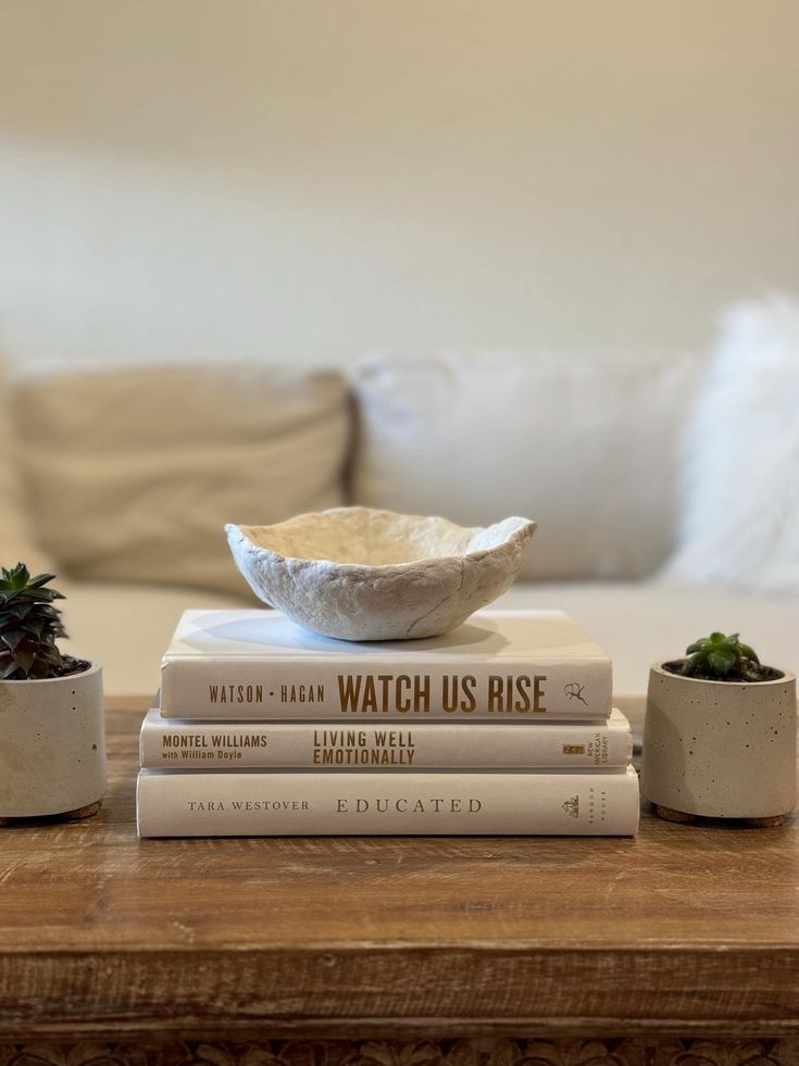 a stack of books sitting on top of a wooden table next to two planters