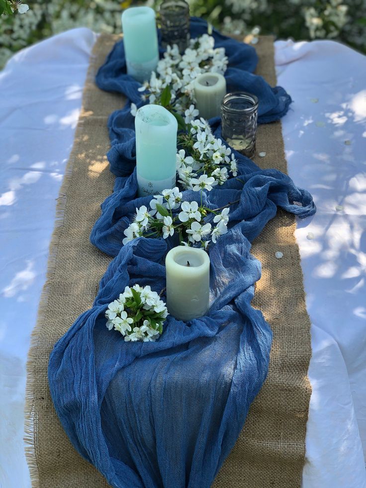 the table is covered with blue cloth and white flowers, candles are placed on each side