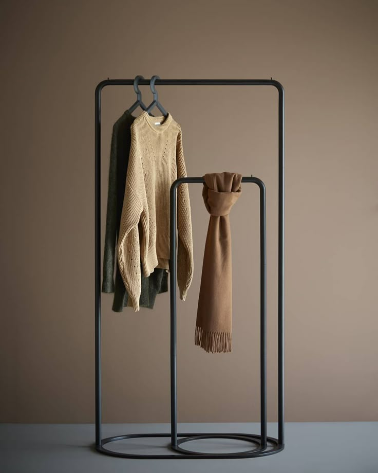 two sweaters and a scarf hanging on a clothes rack