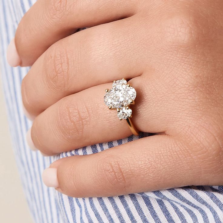 a woman's hand with a diamond ring on her left hand and a striped shirt on the right