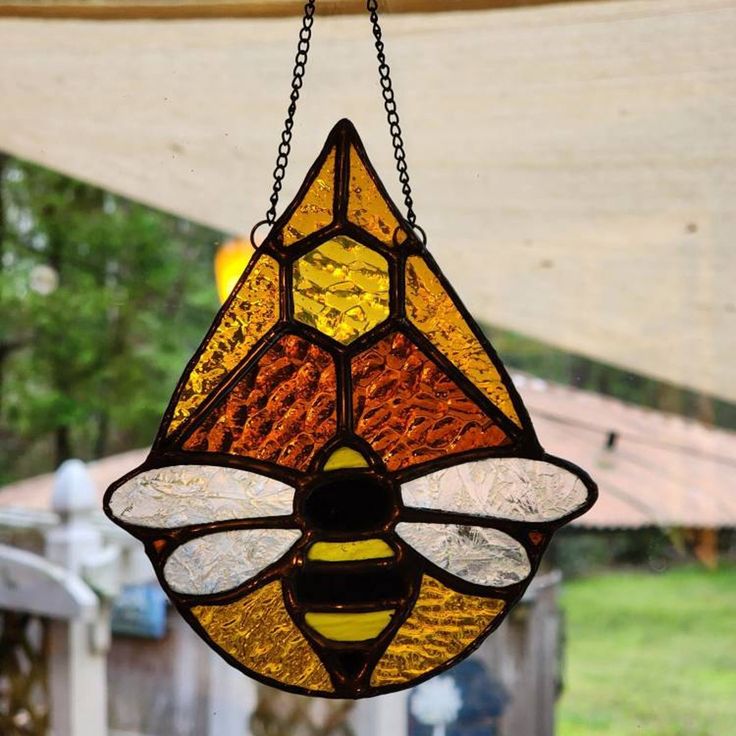 a stained glass hanging light with a bee on it's side and yellow, red, and orange colors