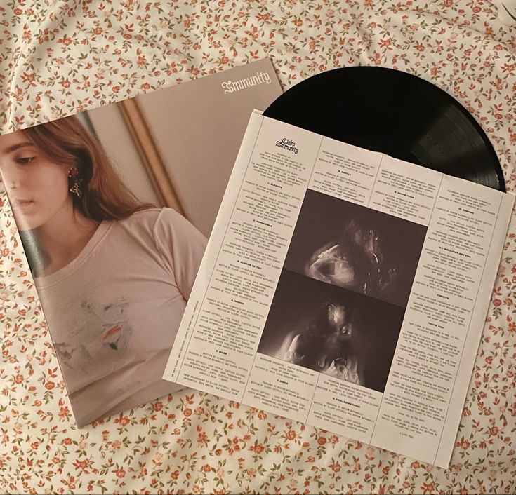 a record player and magazine laying on a floral print tablecloth with an image of a woman's face