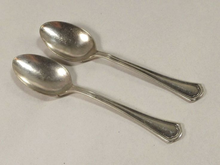 two silver spoons sitting side by side on a white surface