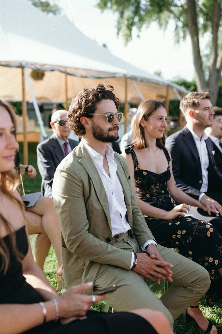 a group of people sitting next to each other on top of a grass covered field