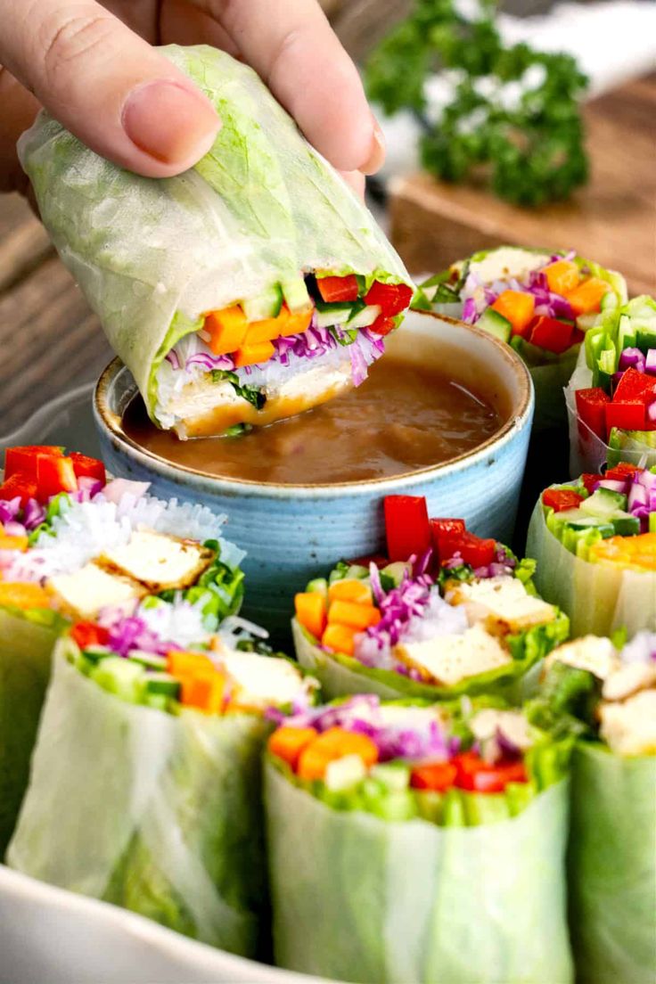 a person dipping some food into a bowl filled with lettuce and other veggies