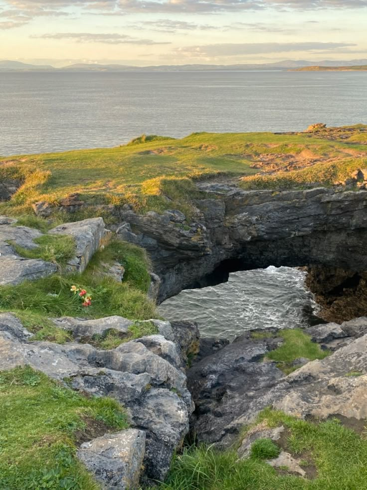 an open hole in the ground with grass and rocks around it, overlooking the ocean