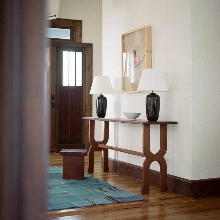 two black vases sitting on top of a wooden table next to a lamp in a room