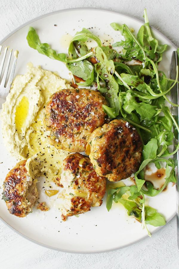 a white plate topped with meat, mashed potatoes and green leafy salad next to a fork