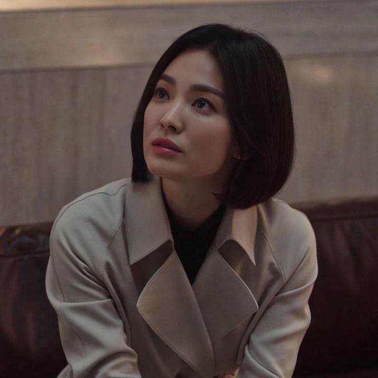 a woman sitting on top of a couch next to a brown leather chair and looking off into the distance