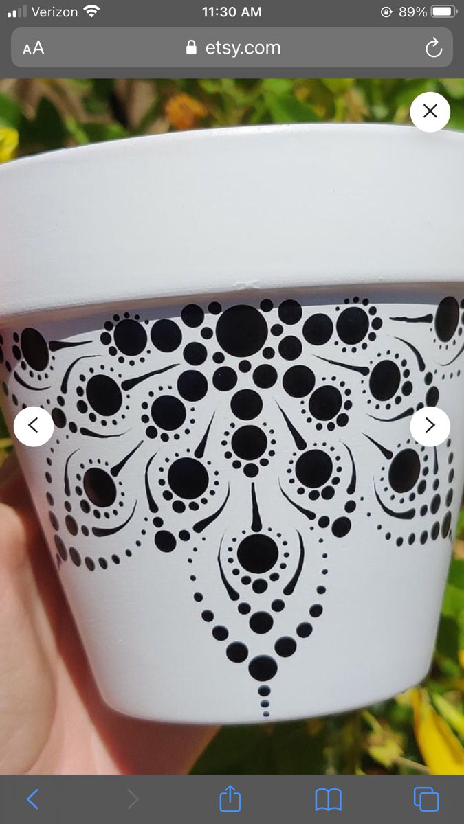 a hand holding a cup with black and white designs on the outside, in front of green plants