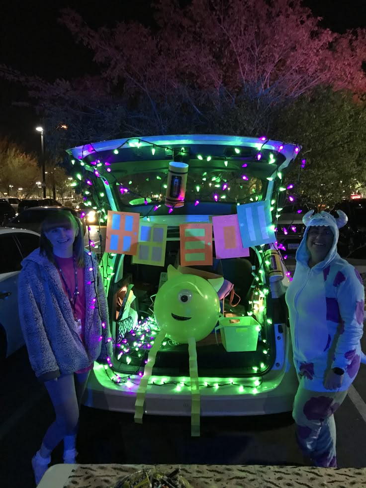 two girls standing in front of a car decorated with christmas lights