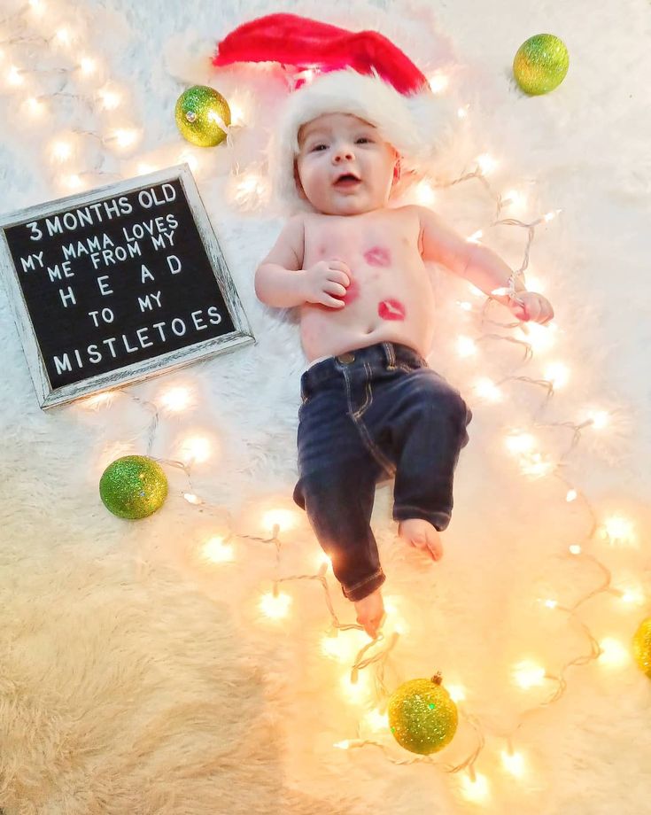 a baby wearing a santa hat laying on top of a white bed covered in christmas lights