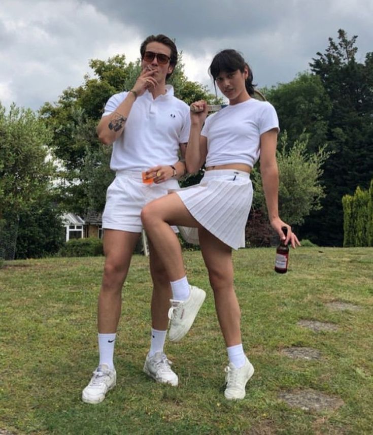 two people dressed in tennis outfits posing for a photo on the grass with beer bottles