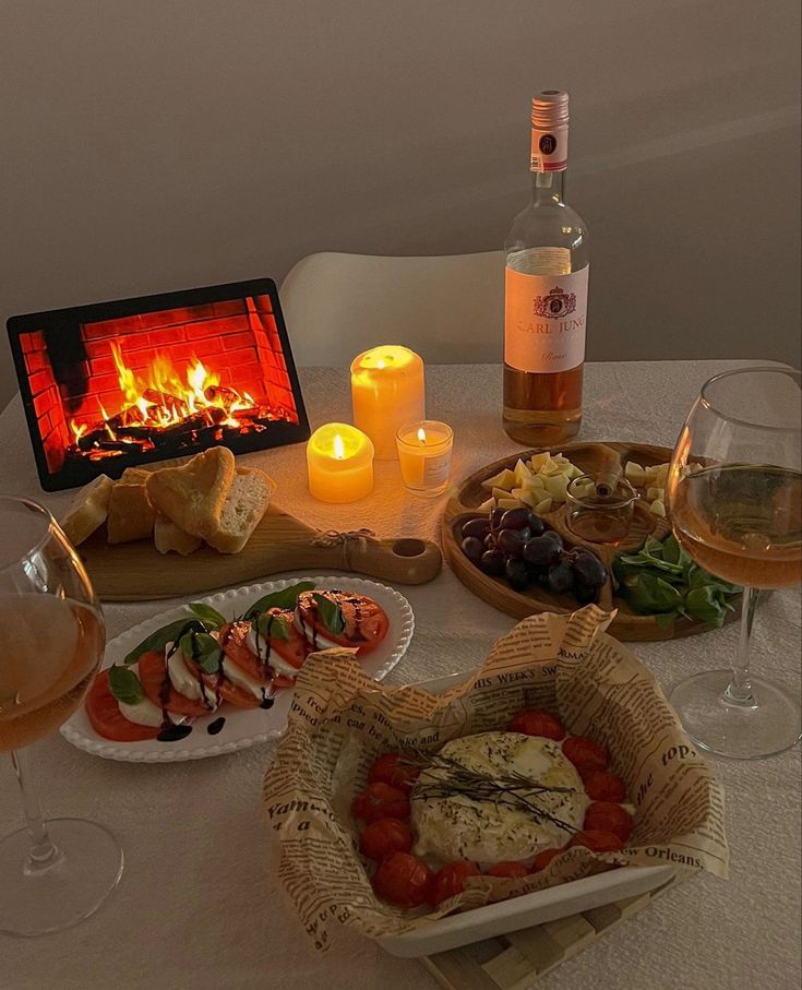 a table topped with wine glasses and plates filled with food next to an open fire