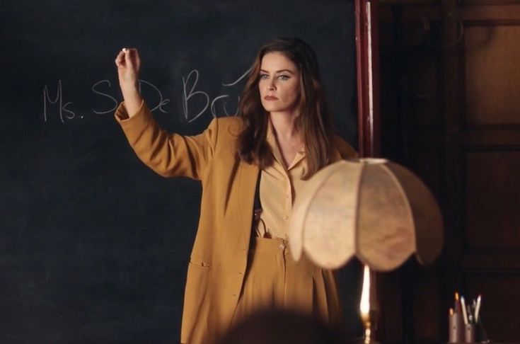 a woman standing in front of a blackboard writing on it