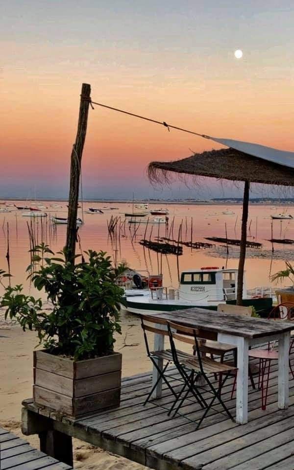 a wooden table sitting on top of a sandy beach next to the ocean at sunset