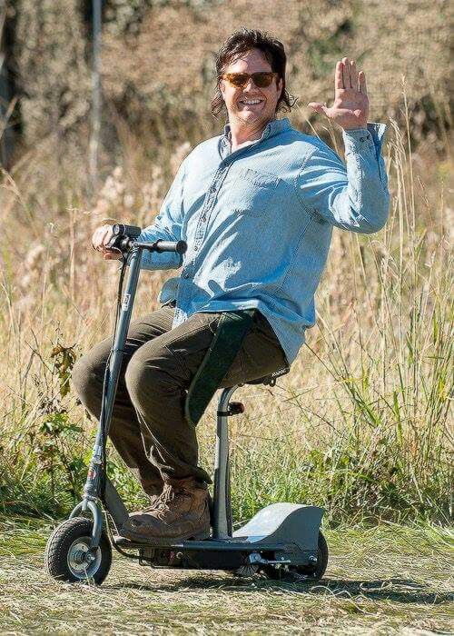 a man is riding an electric scooter in the grass with his hand up