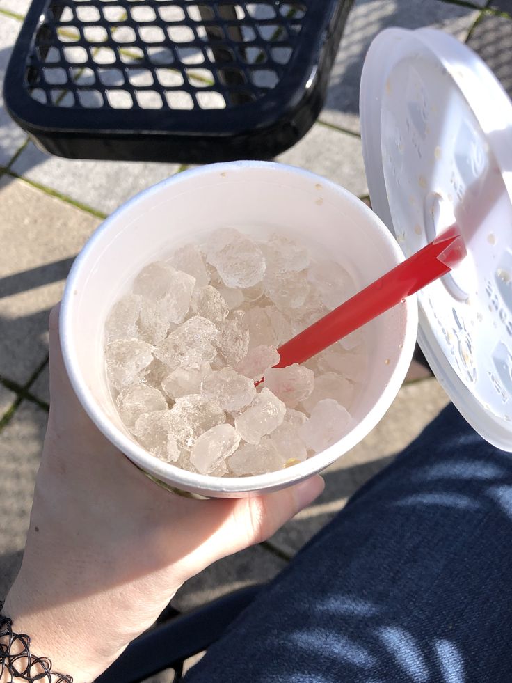 a person holding a cup with ice in it and a red straw sticking out of it